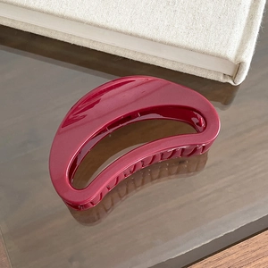 Close-up of a glossy burgundy crescent hair claw clip on a wooden table surface