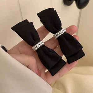 Close-up of black matte satin bow hair clips with rows of white pearl embellishments