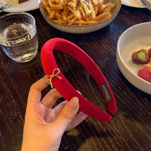 Detail of red velvet headband with gold bow accent and handmade label on side