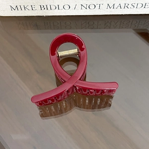 Detail view of burgundy hair claw clip with glossy ribbon cross design and gold spring