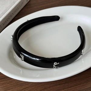 Détail d'un serre-tête en cuir PU noir avec des nœuds argentés sur une assiette blanche