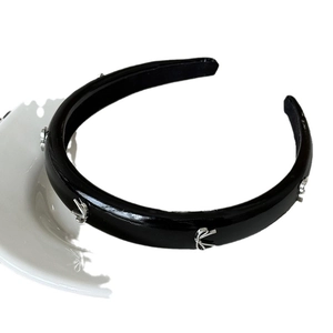 Serre-tête élégant en simili cuir noir avec nœuds métalliques argentés sur assiette blanche