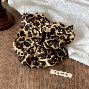 Vue détaillée du chouchou en satin à motif léopard sur un fond en bois sombre