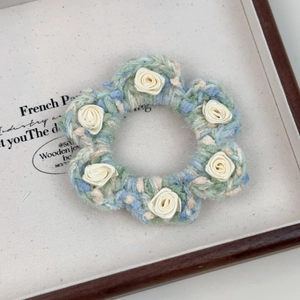 Gros plan d'un chouchou tricoté avec des fleurs en tissu crème sur fond bleu et vert