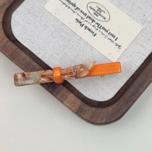 Close-up of orange and marble resin hair clip on a minimalist wooden tray display