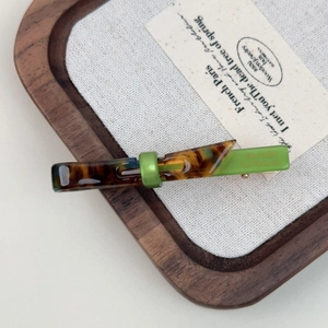 Detail view of marble patterned bow hair clip with dark tortoiseshell and green finish