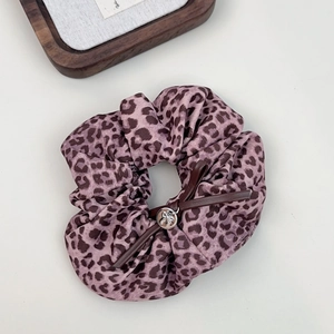 Detailed shot of pink leopard scrunchie with a brown faux leather bow and silver charm