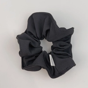Detailed macro view of black ribbed fabric scrunchie with a Hand Made woven label