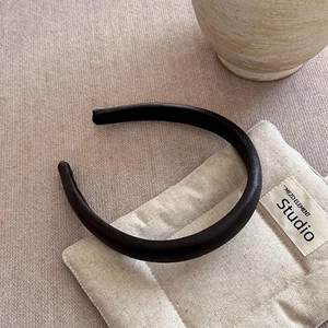 Detail of black faux leather headband with lychee texture on cream fabric background