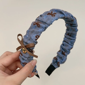 Détail du serre-tête bleu clair avec un nœud marron et un pendentif coeur doré chic