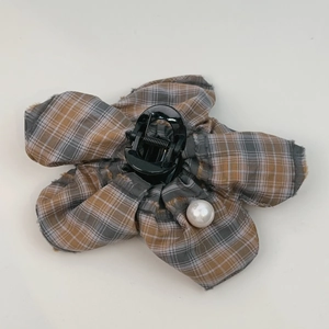 Detailed view of flower-shaped hair claw with retro plaid fabric and a large pearl accent