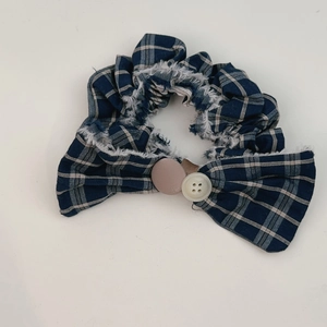 Detail of blue striped scrunchie with button accents, bow design and fringe edges