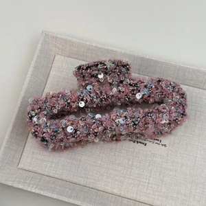 Vue détaillée de dessus d'une pince à cheveux en tweed rose avec des paillettes colorées