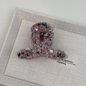 Gros plan d'une pince à cheveux en tweed rose avec paillettes et texture tissée élégante