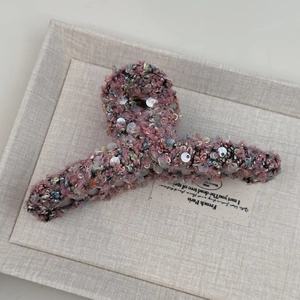 Gros plan sur une grande pince à cheveux en tweed rose avec des paillettes brillantes