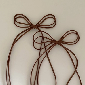 Detail of two brown suede bow hair clips with long streamers on a cream background