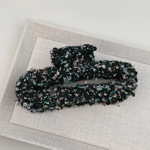 Détail d'une pince à cheveux en tweed avec paillettes noires et fils brillants sur plateau