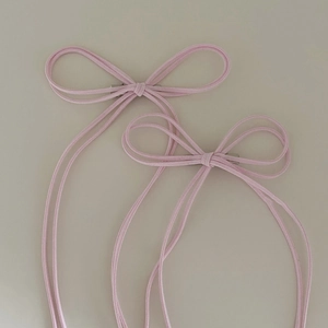 Detail of two pink ribbon bow hair clips with silver metal duckbill clips on beige fabric