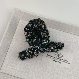 Détail d'une pince à cheveux en tweed noir à paillettes style français sur plateau gris