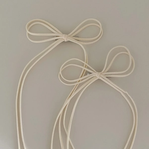 Detail of two cream white suede bow hair clips with delicate tassels and silver clips