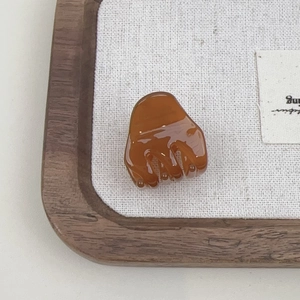 Macro shot of amber acetate hair claw clip showing glossy finish on a wooden tray