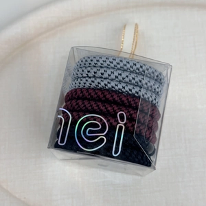Macro detail of high-elastic woven hair ties in dark grey and black within a clear box