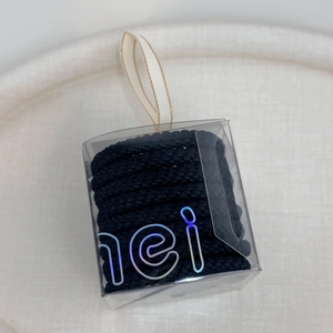 Detail of black high-elastic hair ties in a clear square gift box with a silk ribbon handle