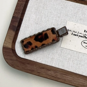 Macro detail of wave-edge leopard print hair clip on a minimalist wooden display