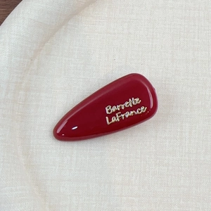 Gros plan sur une pince à cheveux bordeaux avec inscription Barrette LaFrance dorée