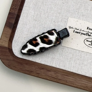 Detail of leopard print hair clip with black metal base on a textured wood tray