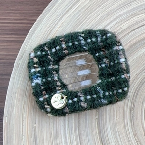 Detail view of dark green tweed hair claw with golden bow charm on a wooden background