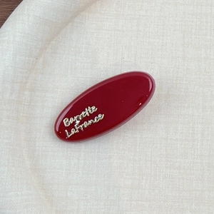 Détail d'une barrette ovale en résine bordeaux avec lettrage doré Barrette La France