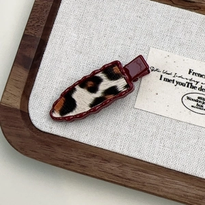 Close-up of leopard print hair clip with burgundy wavy border on rustic background