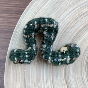 Detail view of dark green tweed hair claw clip with golden star pendant on wood tray