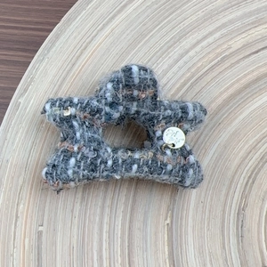 Detail of tweed star hair claw with golden metal pendant on light wood tray