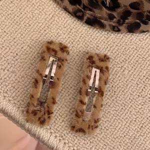 Détail de deux barrettes en peluche à motif léopard sur un fond en maille beige doux