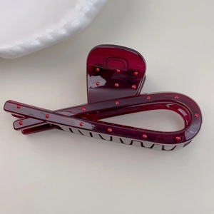 Macro view of dark red polka dot hair claw clip on a minimal ceramic dish background