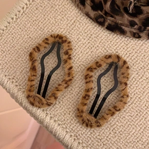 Détail de deux barrettes BB en peluche avec motif léopard sur un fond beige texturé