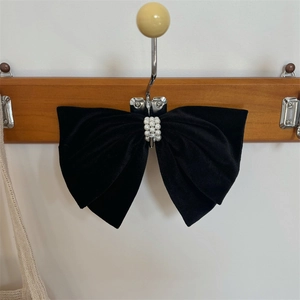 Elegant black velvet bow hair clip with white pearls hanging on a wooden hook