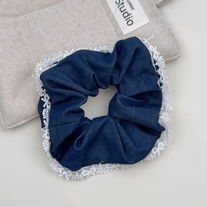 Nahaufnahme von blauem Denim-Haargummi mit eleganter weißer Spitze auf beige Stoff