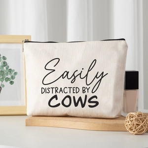Linen style cow print makeup bag with black zipper on rustic wooden stand