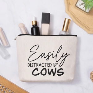 Linen style cow slogan makeup bag with silver zipper on white marble background