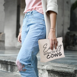 Close-up of linen cow pattern makeup bag with 'Easily Distracted by Cows' text and zipper