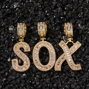 Gold-plated letter pendants S, O, X with baguette zircon stones on black gravel background