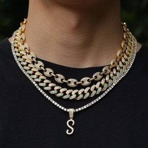 Close-up of iced out layered necklaces with golden chains and zircon S letter pendant