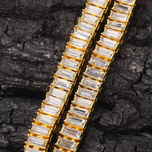 Close-up of golden tennis chain with baguette-cut stones on dark textured charcoal