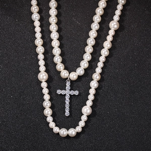 Detalle de collar de perlas de doble capa con colgante de cruz de circón sobre fondo negro