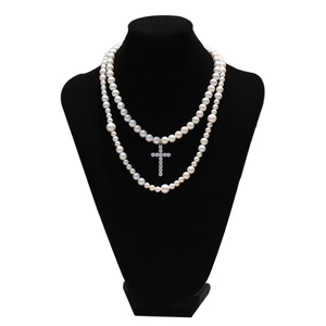 Detalle de collar de perlas de doble capa con un colgante de cruz de circonio plateado