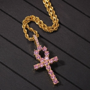 Detailed shot of gold Ankh pendant with pink zircons on rope chain over dark wood background