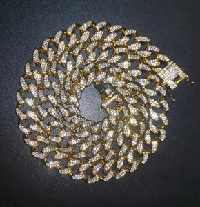 Close-up of gold iced out 13mm Cuban link chain with square diamond clasp on black leather